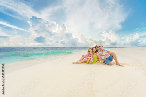  A family with two toddler children sit on sand beach on summer holiday.