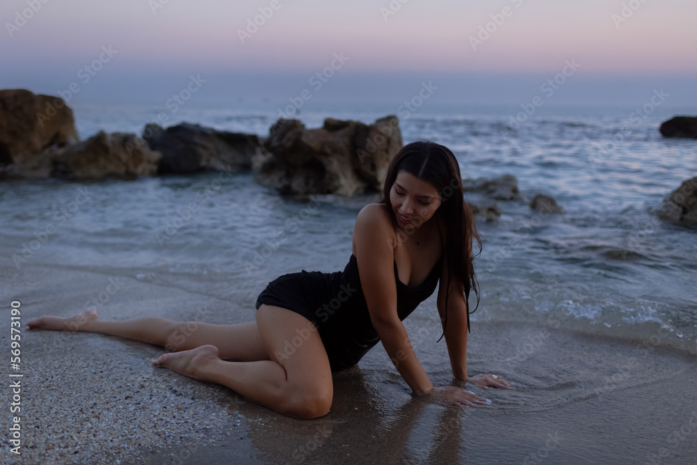 A beautiful woman in a black dress lies on the beach and looks away while relaxing by the sea in summer. A beautiful woman in a black dress lies on the beach and looks away while relaxing by the sea in summer.