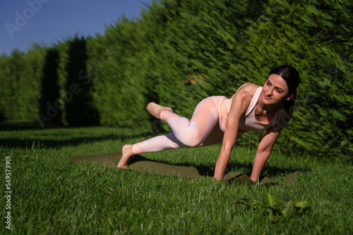 A girl is engaged in yoga on the street, in a pink tracksuit does various exercises and yoga poses