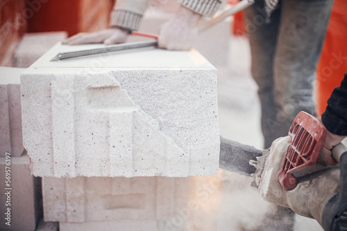 Workers cutting autoclaved aerated concrete block with chainsaw closeup. Builders cutting white blocks for masonry installation. Process of house building at construction site. photo