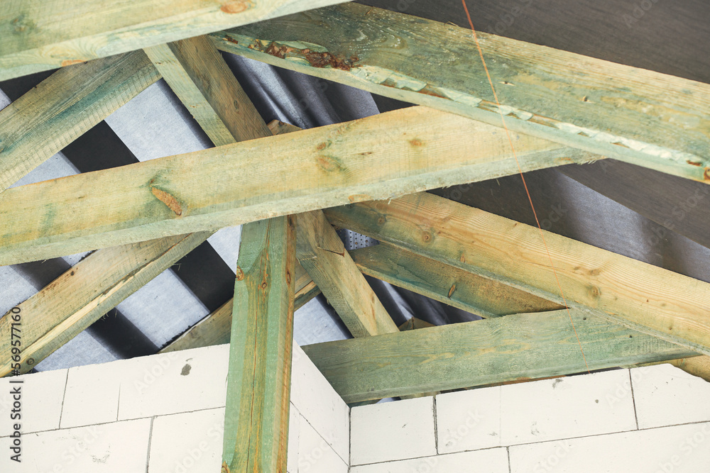 Unfinished attic wooden roof framing with vapor barrier close up. View on timber rafters and beams on aerated concrete blocks in mansard. New modern farmhouse construction Unfinished attic wooden roof framing with vapor barrier close up. View on timber rafters and beams on aerated concrete blocks in mansard. New modern farmhouse construction