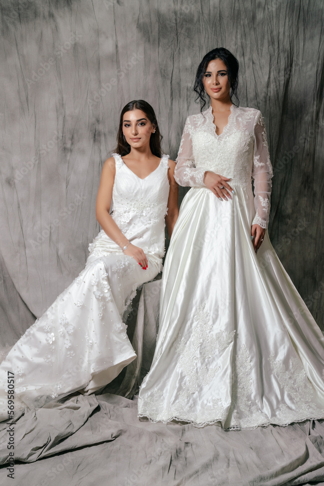 Two girls in a wedding dress studio portrait on a gray background