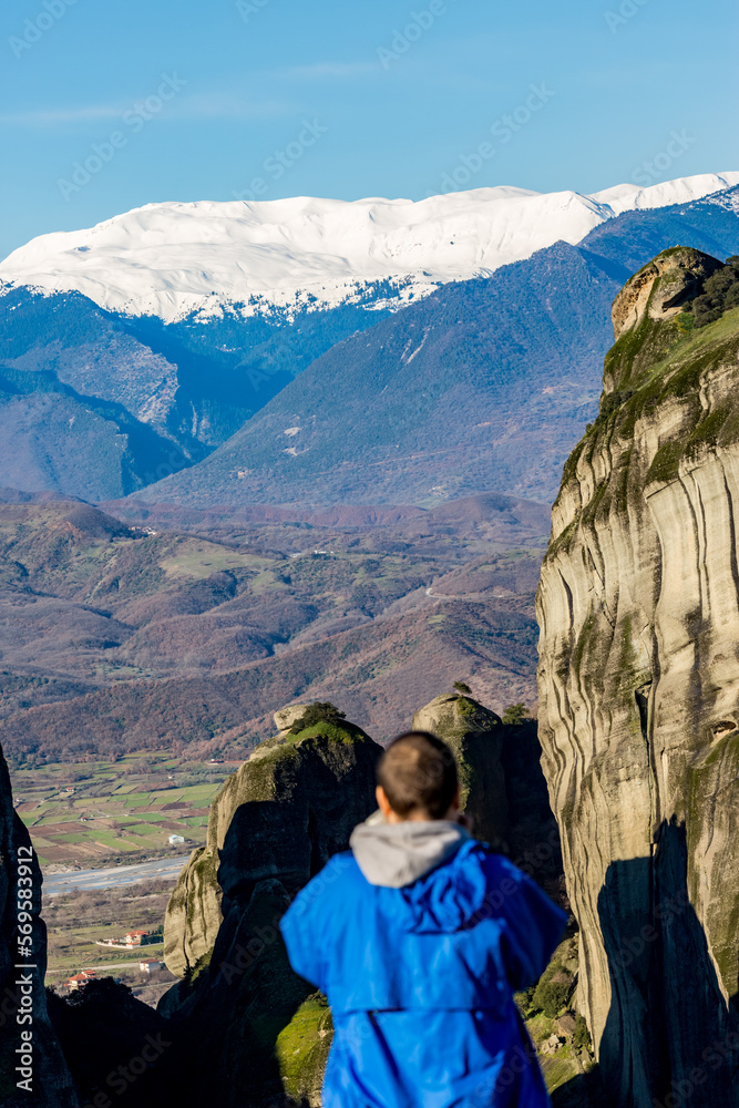 Naklejka premium Scenery sunny day panoramic view, the cliffs of Meteora, Greece with a blurred defocused male figure with blue raincoat