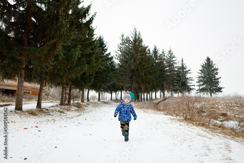 A 3-year-old boy runs in the snow in winter and rejoices in his childhood. Warm winter clothes. Copy space