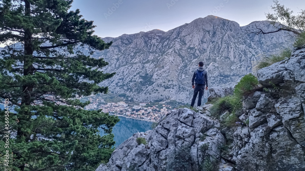 Rear view of man with backpack on rock looking at scenic view near Vrmac Sveti Ilija in summer, Adriatic Mediterranean Sea, Montenegro, Balkans, Europe. Hiking trail in Kotor bay, Dinaric Alps