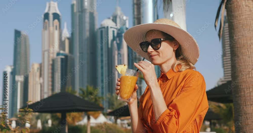 attractive woman in orange dress and sun hat drinks smoothie cocktail at Dubai beach resort. vacations in UAE