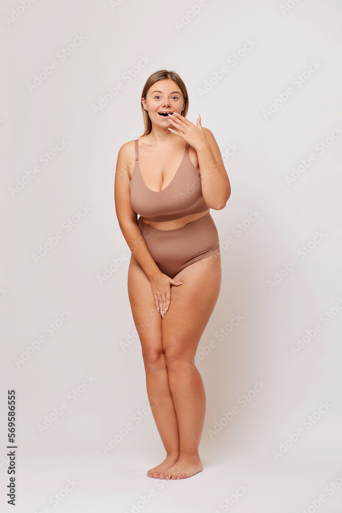 Obraz premium Full lengths shot of positive surprisedEuropean brunette woman in her 30s covers wide opened mouth in shock can not believe her own eyes wears beige underwear. Body positive concept 
