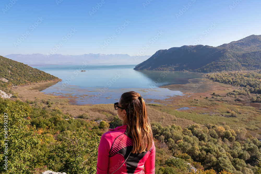Rear view of woman with panoramic view of Lake Skadar National Park in autumn seen from Virpazar, Bar, Montenegro, Balkans, Europe. Stunning travel destination in Dinaric Alps near Albanian border