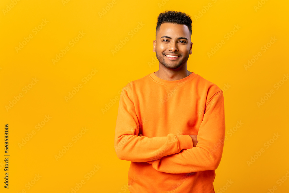 Portrait of happy satisfied handsome indian young man in casual wear standing with crossed arms and looking at camera with toothy smile. Indoor studio shot on orange background Portrait of happy satisfied handsome indian young man in casual wear standing with crossed arms and looking at camera with toothy smile. Indoor studio shot on orange background