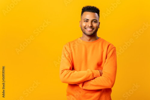 Canvas Print Portrait of happy satisfied handsome indian young man in casual wear standing with crossed arms and looking at camera with toothy smile