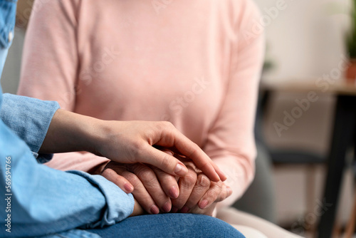 Old woman and her daughter holding hands close up view. Woman expressing care as psychological support to retired lady