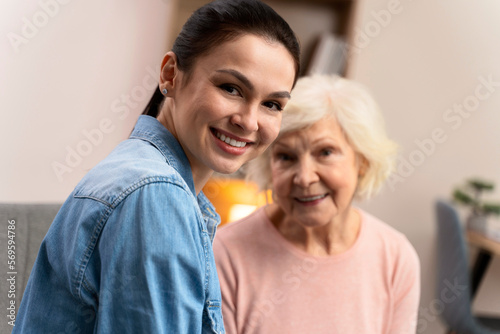 Loving adult daughter posing with happy old mother at the sofa at home. Empathy and care to elderly people concept