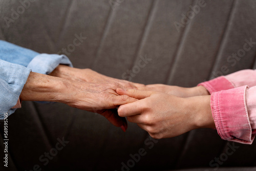 Cropped view of the hands of old woman and her daughter at the sofa background. Family relationships concept