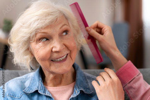 Cropped view of the cute senior woman smiling while her daughter comb her hair and make hairstyle on sofa at home. Stock photo
