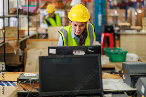 Young female asian worker doing her daily routine in the warehouse. She is wearing reflective vest and hard hat.