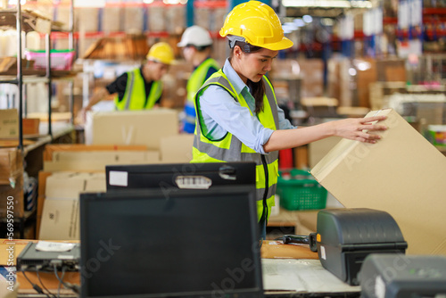 Young female asian worker doing her daily routine in the warehouse. She is wearing reflective vest and hard hat.