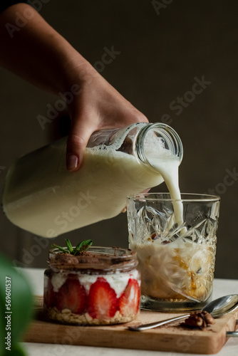 A girl pours milk into a glass with frozen coffee next to tirramisu with strawberries photo