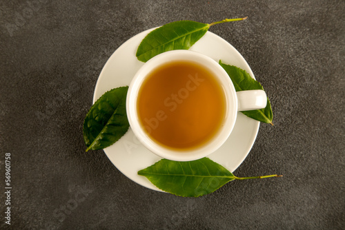 A glass cup of green tea, tea leaves and lemons, on black background 