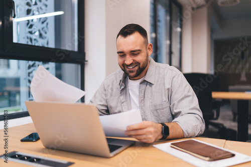 Smiling businessman having paperwork while using computer © BullRun