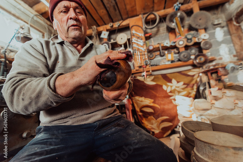 A senior man sitstingin the workshop and smearsing wooden utensils with linseed oil