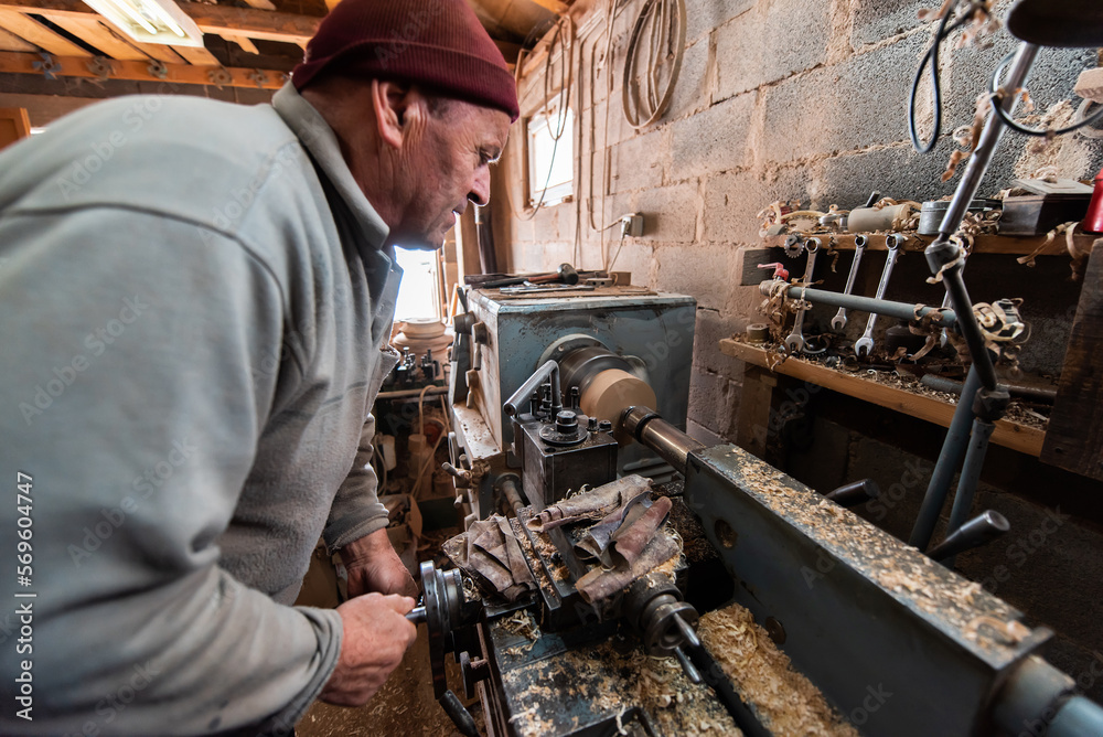 A senior man procesing wood on a lathe and making wooden dishes in the workshop