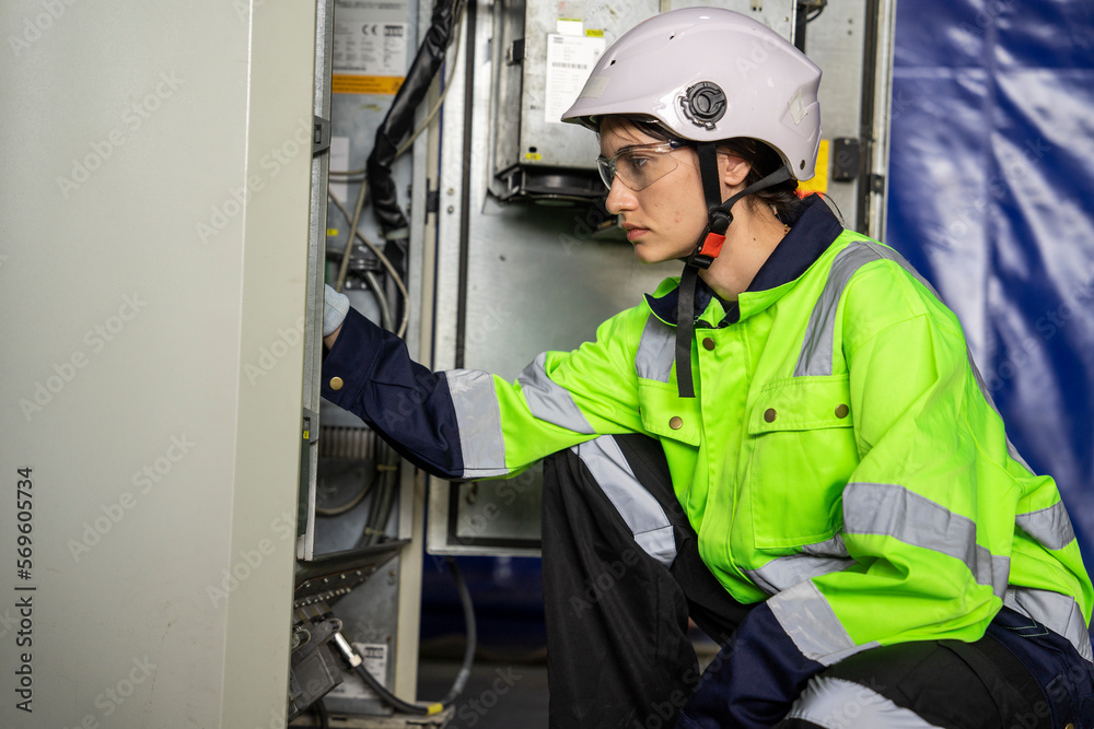 Female electrician inspecting electrical system inside factory sitting at electrical control box Female electrician inspecting electrical system inside factory sitting at electrical control box