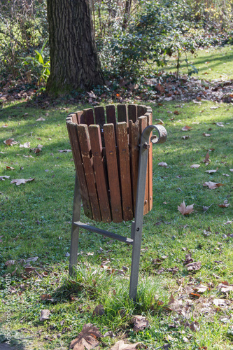 a wooden trash bin in a park surrounded by dry leaves