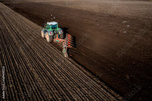 Obraz na plátně Aerial view of a tractor ploughing a fertile field with scavenging birds in flig