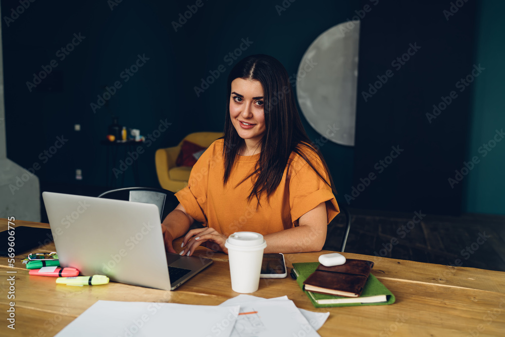 Smiling woman working on laptop at table in dark room Smiling woman working on laptop at table in dark room