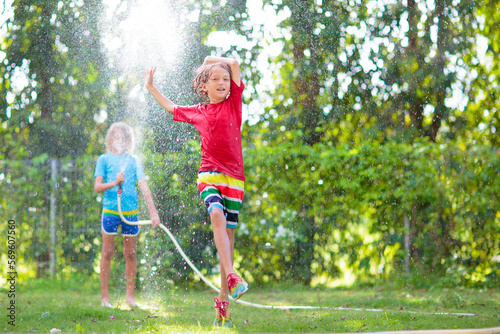 Kids play with water sprinkle hose. Summer garden