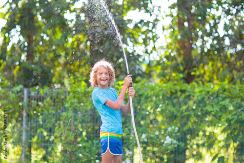 Kids play with water sprinkle hose. Summer garden