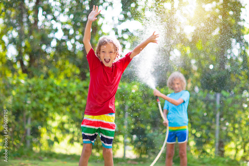 Kids play with water sprinkle hose. Summer garden © famveldman
