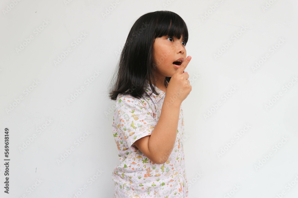 Surprised little girl wearing pajama looking at copy space while pointing with hand, isolated on the grey background Surprised little girl wearing pajama looking at copy space while pointing with hand, isolated on the grey background