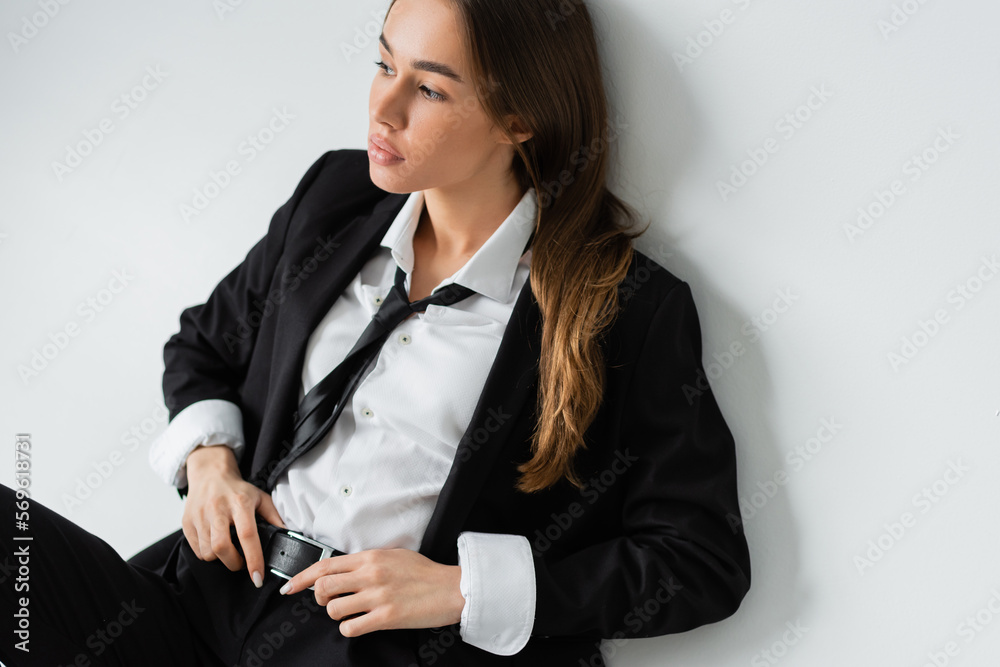 high angle view of young brunette woman in black formal wear touching belt on grey background. high angle view of young brunette woman in black formal wear touching belt on grey background.