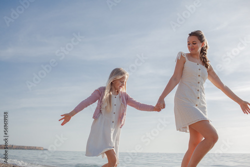 Mither holds the doughter hand and walks in the baech together against the background the sea or coean photo