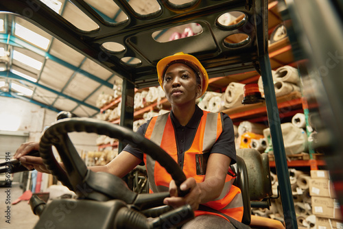 Young African female forklift operator driving around a warehouse