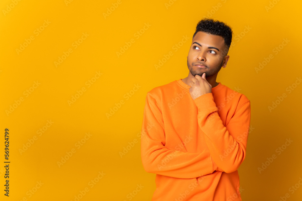 Fototapeta premium Pensive indian man holding hand near chin and thinking about something, looking for new idea or solution, trying to recall some important thing, puzzled multiracial guy isolated on yellow