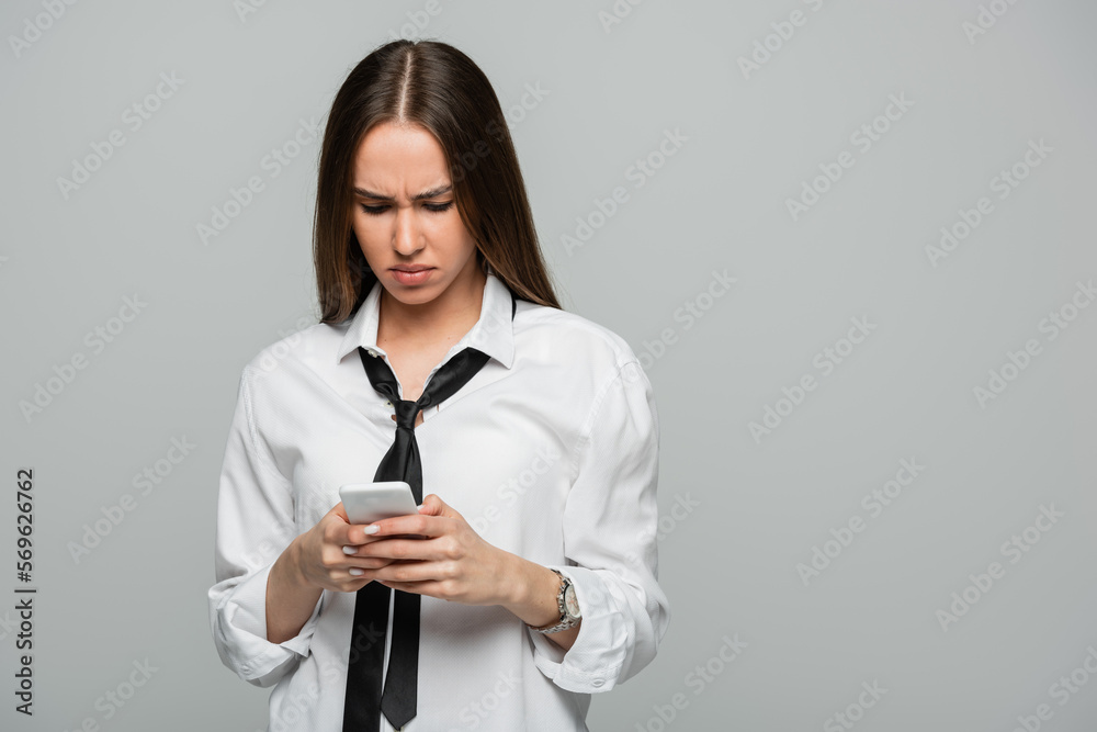 young woman in white shirt and tie messaging on smartphone isolated on grey. young woman in white shirt and tie messaging on smartphone isolated on grey.