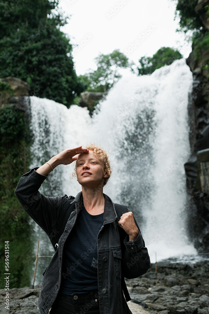 A young blonde girl with a backpack travels to a large waterfall. A young blonde girl with a backpack travels to a large waterfall.