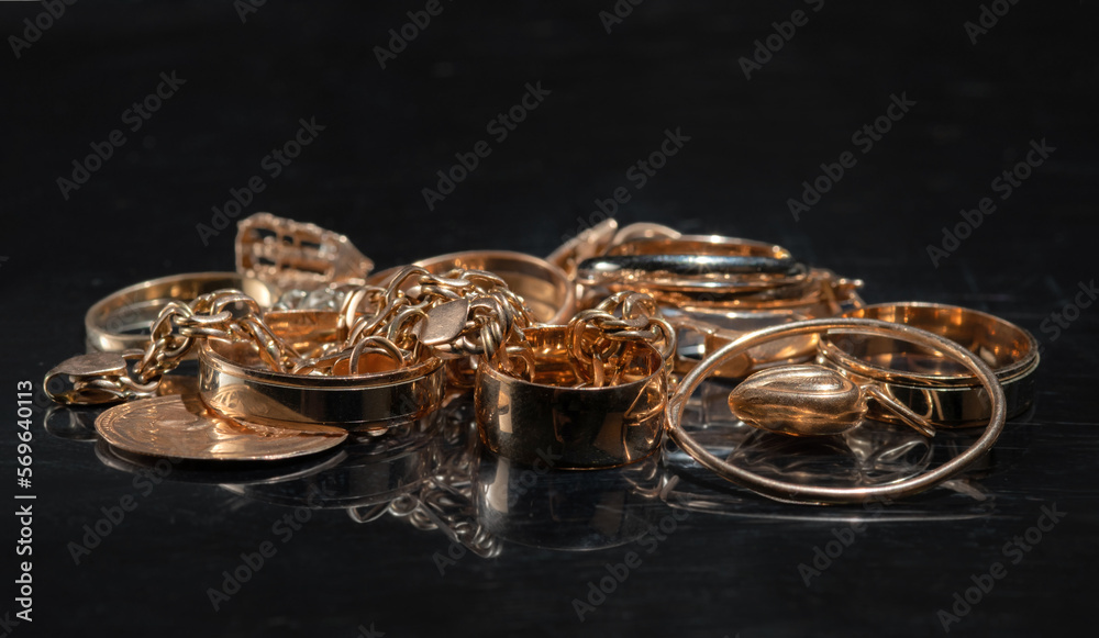 A bunch of different gold jewelry on a mirror black background. Selective focus. A bunch of different gold jewelry on a mirror black background. Selective focus.