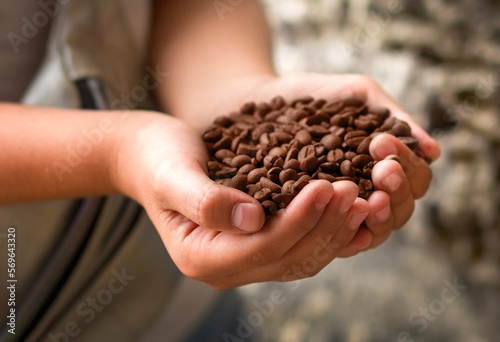 A handful of roasted, brown, fragrant coffee beans in the children's palms of a 10-year-old girl who wants to smell the smell of coffee. Selective focus on the fingers and part of the grains