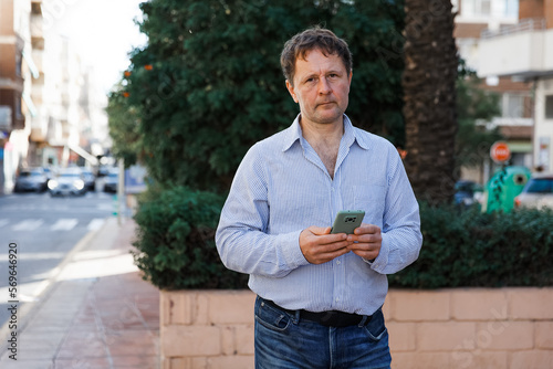 A serious businessman man talks on a mobile phone on the street, in the city