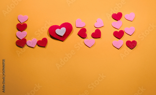 The inscription love is laid out on a yellow background of small pink and red hearts. Top view. The concept of Valentine's Day. With copy space.