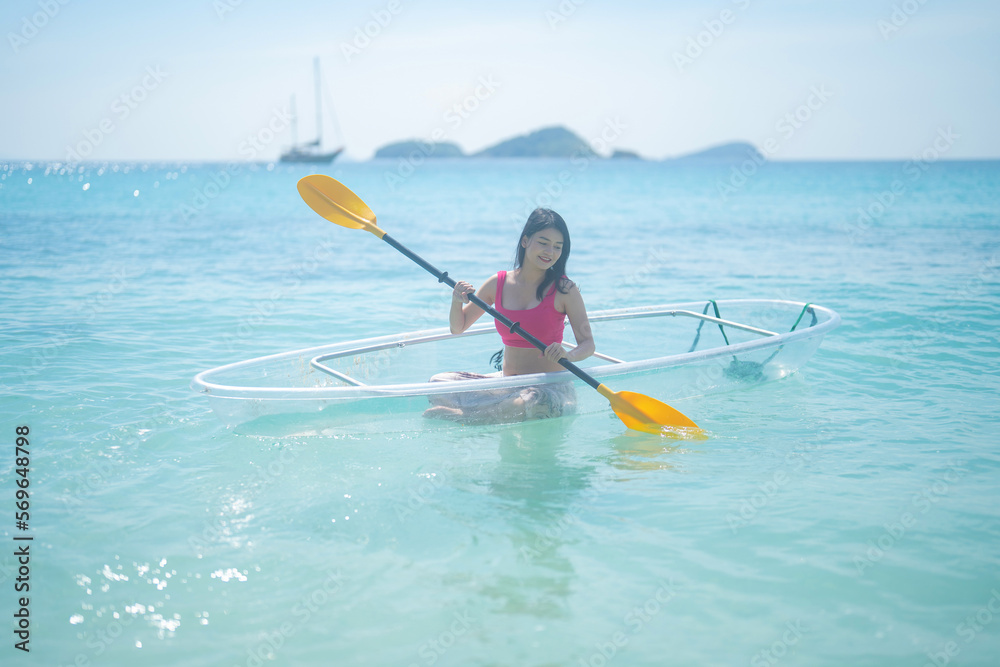 An Asian woman, a tourist, paddling a boat, canoe, kayak or surfboard with clear blue turquoise seawater, Andaman sea in Phuket island in summer season, Thailand. Water in ocean