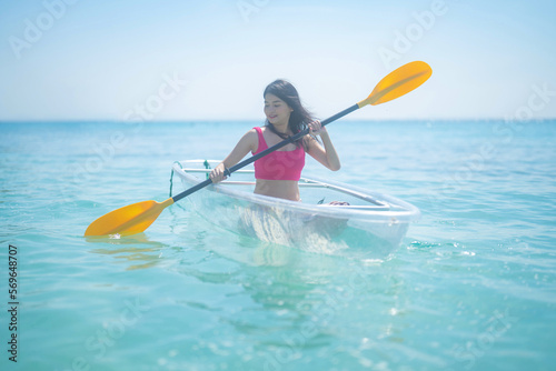 An Asian woman, a tourist, paddling a boat, canoe, kayak or surfboard with clear blue turquoise seawater, Andaman sea in Phuket island in summer season, Thailand. Water in ocean