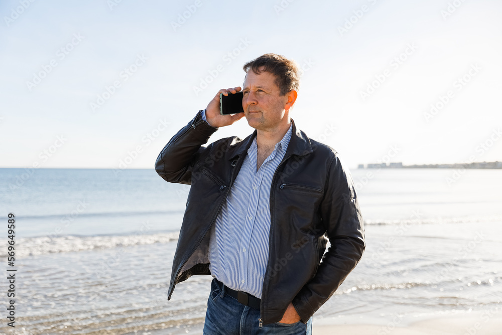 Businessman Talking On Phone, using smartphone mobile apps texting message, surfing social media tech standing on the city beach against the backdrop of the sea Businessman Talking On Phone, using smartphone mobile apps texting message, surfing social media tech standing on the city beach against the backdrop of the sea