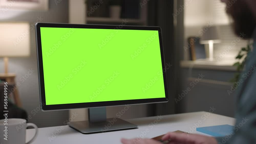 Mature bearded man working on personal computer at home, cozy evening typing on keyboard, close up of green chromakey monitor Mature bearded man working on personal computer at home, cozy evening typing on keyboard, close up of green chromakey monitor