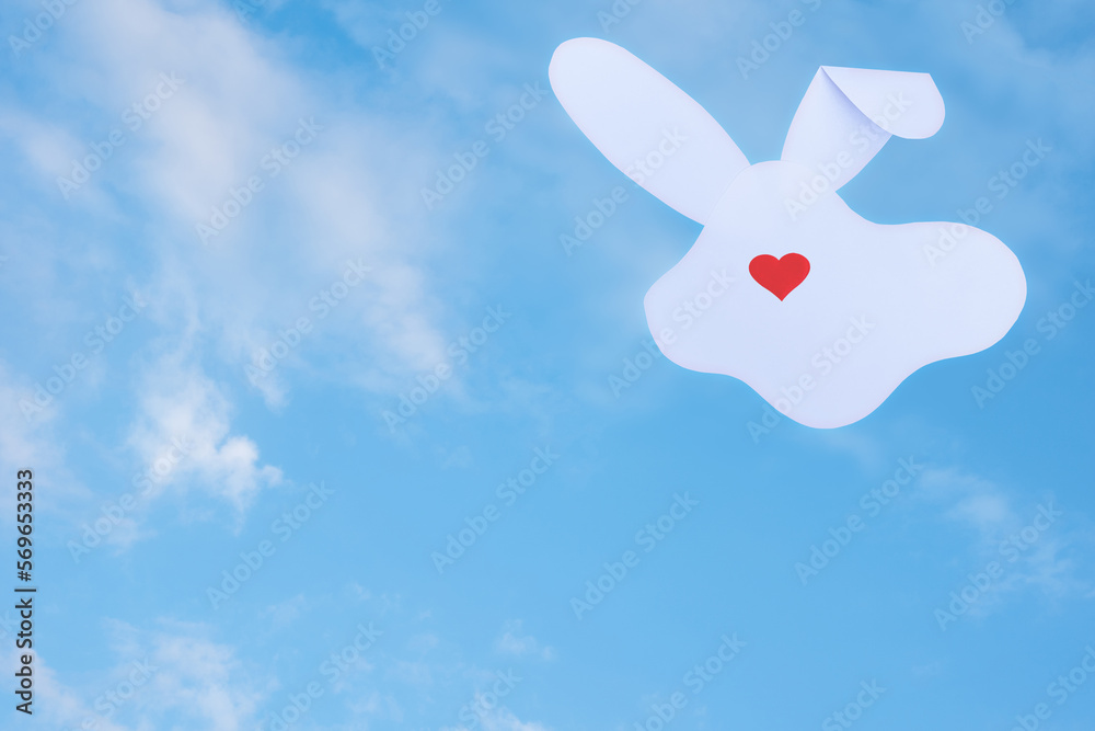 Creative card made of silhouette of a white paper rabbit and a red heart instead of a nose on a cloudy sky background Creative card made of silhouette of a white paper rabbit and a red heart instead of a nose on a cloudy sky background
