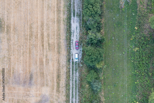 two cars are standing on the road between two fields. Fields of green and yellow. Drone photo