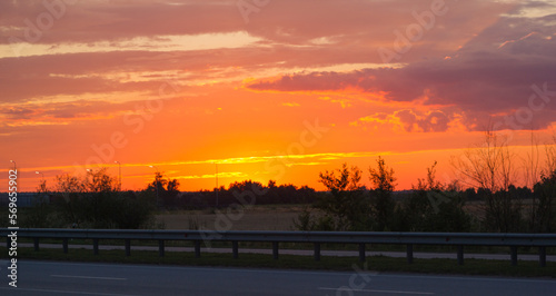 photo of the autobahn against the backdrop of a bright orange sunset sky. Steppe with shrubs along the route